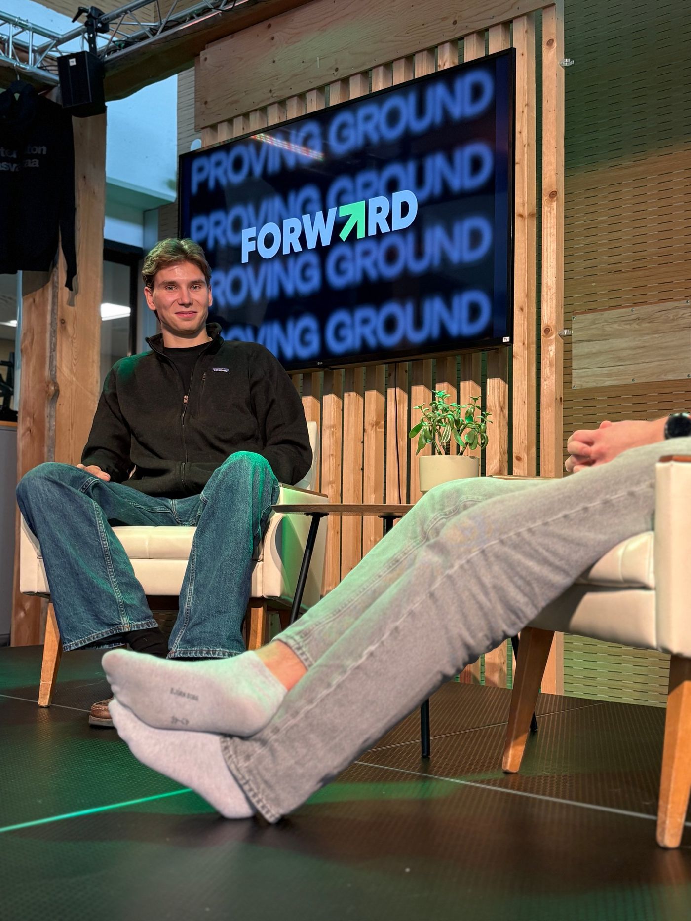 Two chairs and a microphone in front of a Proving Ground / FORW7RD screen.