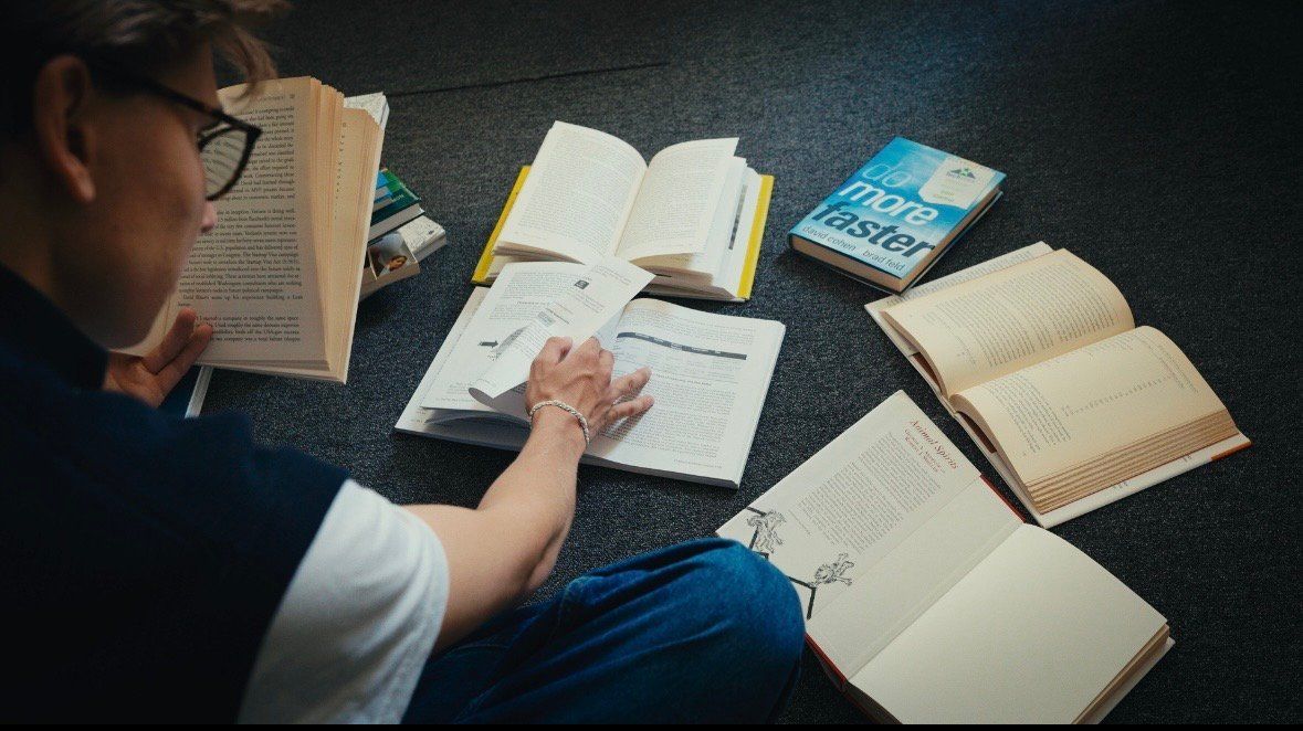 A reader working through open strategy books spread across a dark carpet.